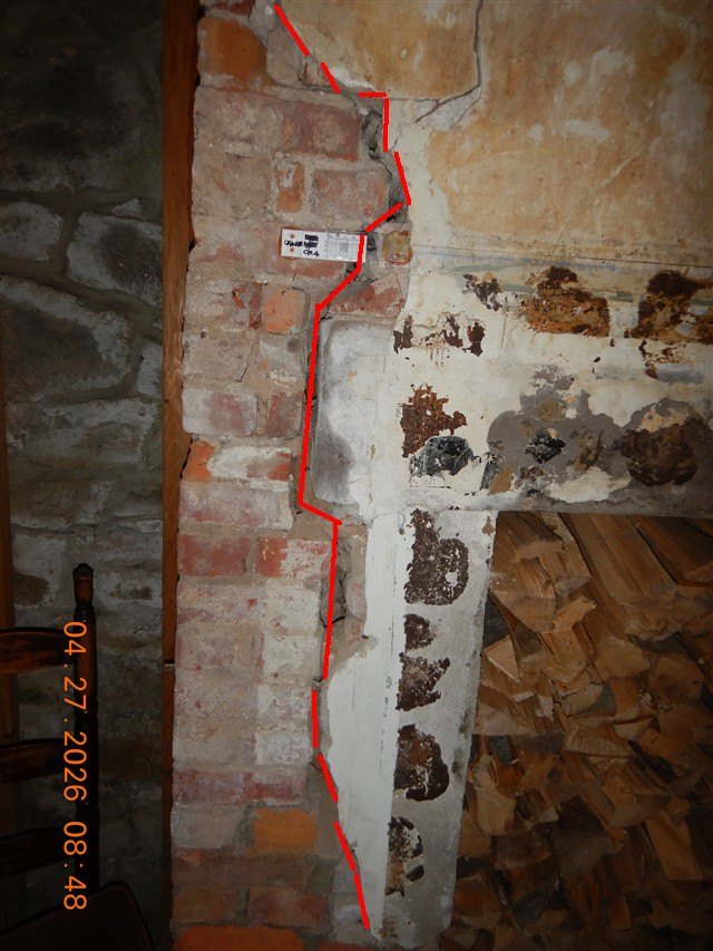 Interior brick masonry with a long vertical crack traced in red, firewood stacked beside it